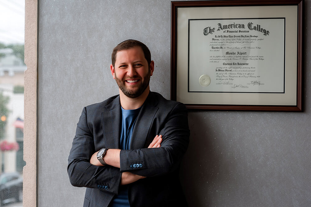 Moshe Alpert, standing next to his diploma hanging on the wall