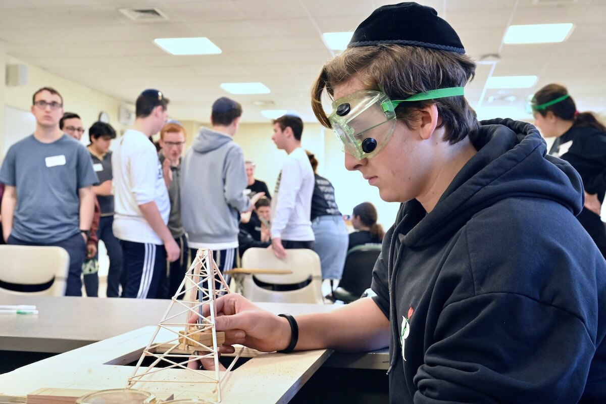 A student wearing goggles fixes a pyramid-esque science experiment