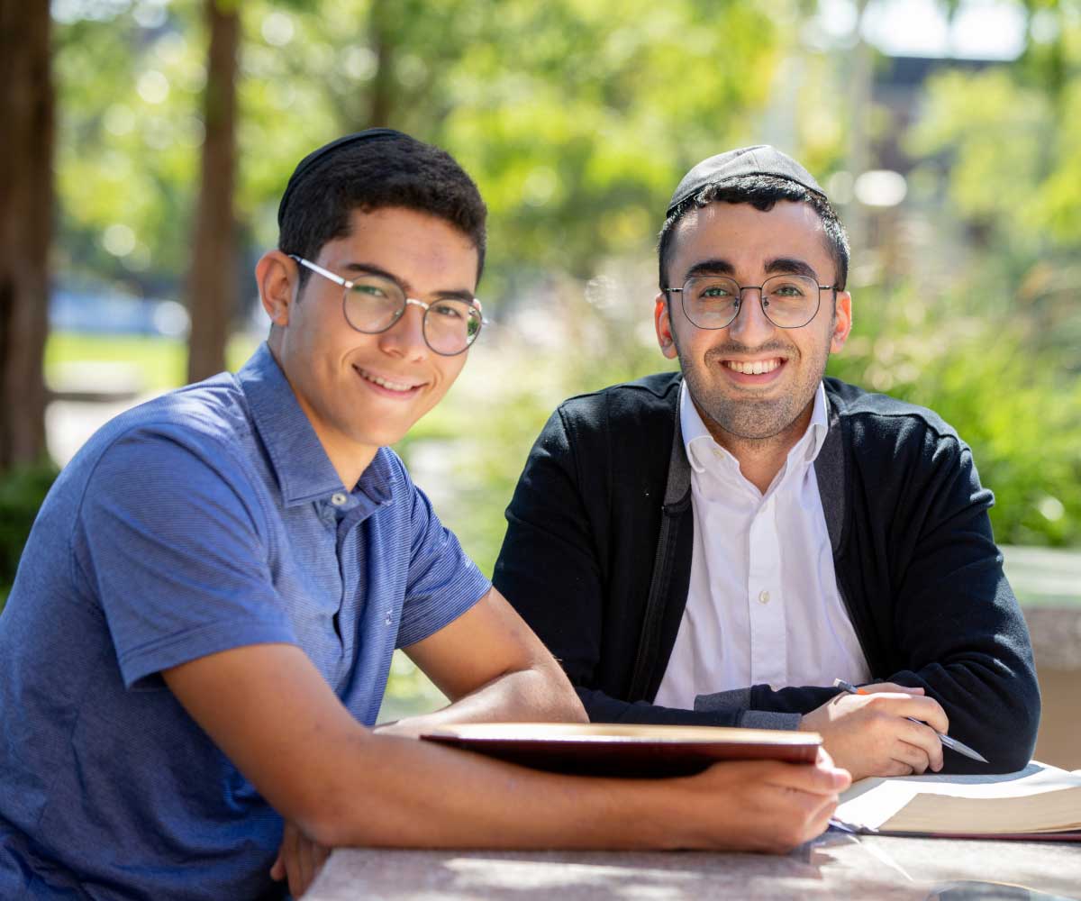 Student sitting outside in a lush, green space on campus with upperclassman mentor