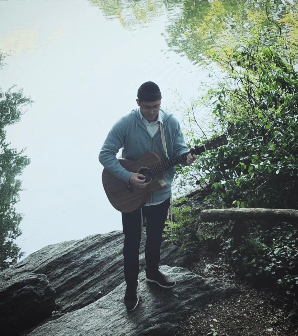 Lander College student Shlomo Ganz playing his guitar by a body of water.