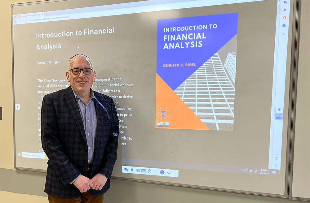Dr. Kenneth Bigel standing in front of a smartboard with the cover of his online textbook "Introduction to Financial Analysis on the screen. 